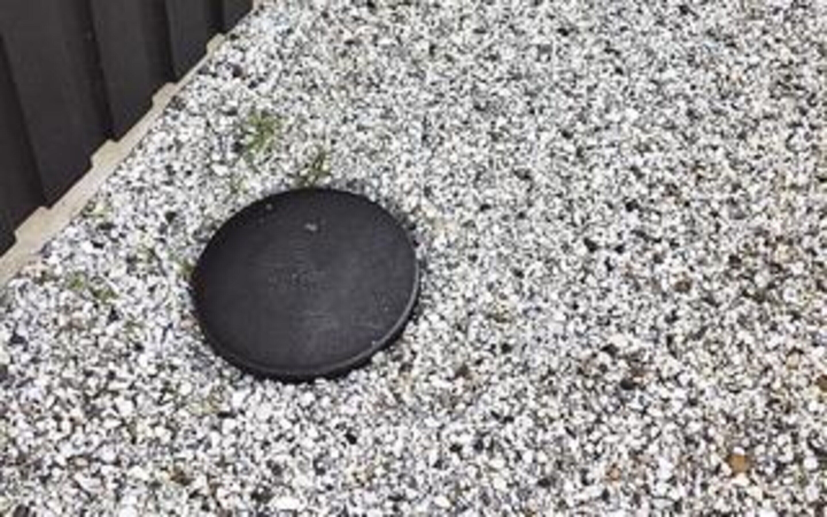 Un objet rond, de couleur sombre, posé sur une surface de gravier.