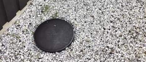 Un objet rond, de couleur sombre, posé sur une surface de gravier.