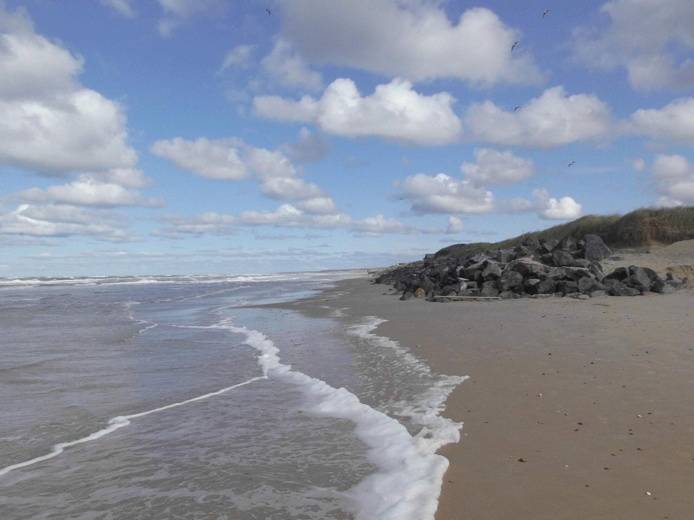 Une plage avec des vagues, un ciel dégagé et quelques rochers.