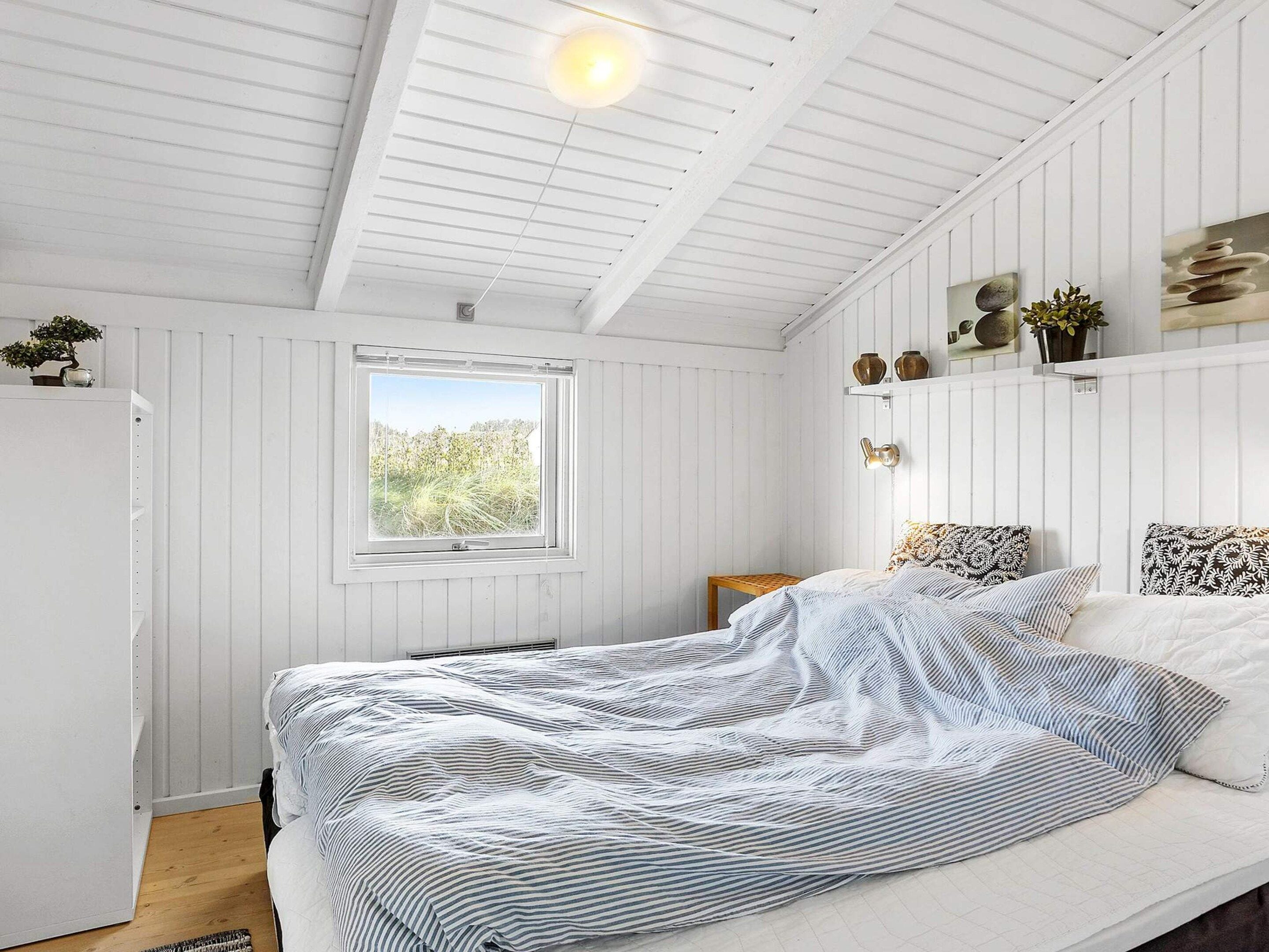 A bedroom with a bed, a window, and a wall-mounted shelf with decorative items.