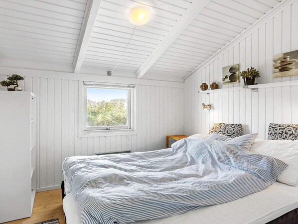 A bedroom with a bed, a window, and a wall-mounted shelf with decorative items.