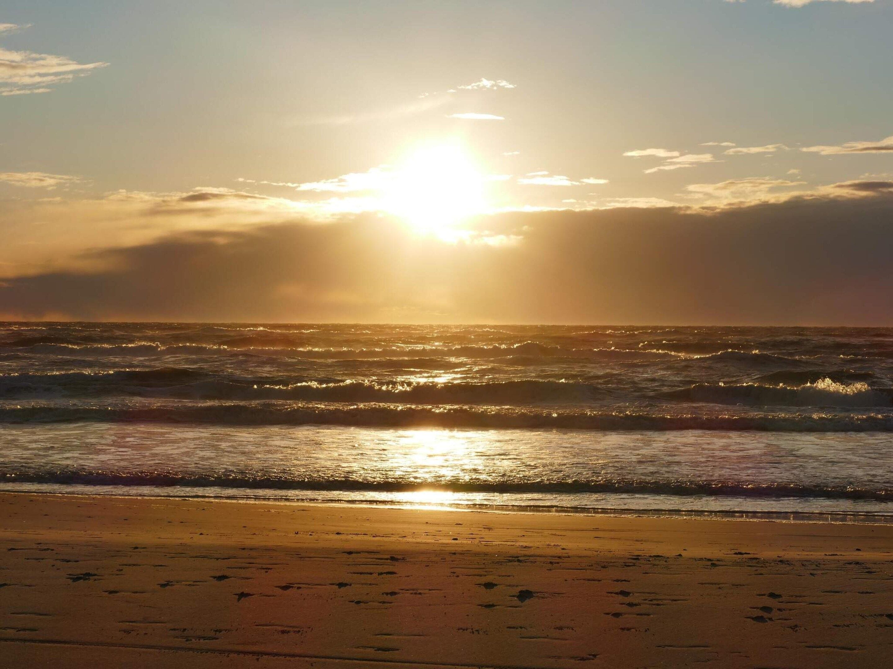 A beach with waves and the sun setting over the horizon.