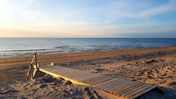 A beach with a wooden boardwalk leading to the water, footprints in the sand, and a clear sky.