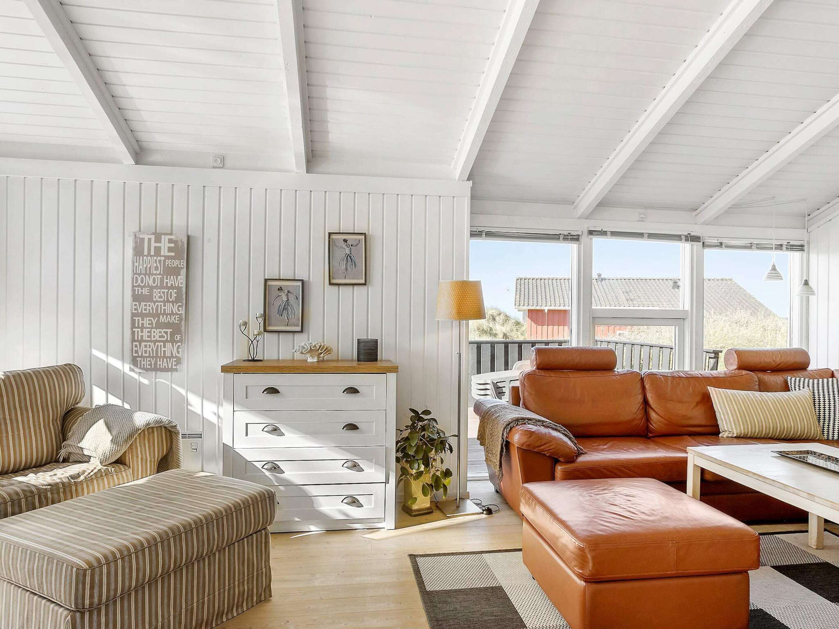 A spacious living room with a white wooden ceiling, a sofa set, a coffee table, and a side table with decorative items.