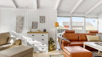 A spacious living room with a white wooden ceiling, a sofa set, a coffee table, and a side table with decorative items.