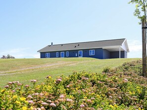 Une maison de plain-pied avec un toit plat, une véranda et un jardin devant la maison agrémenté de plantes à fleurs.