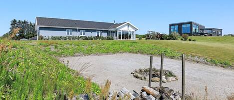 A modern house with a large patio area, surrounded by a grassy field and a gravel path.
