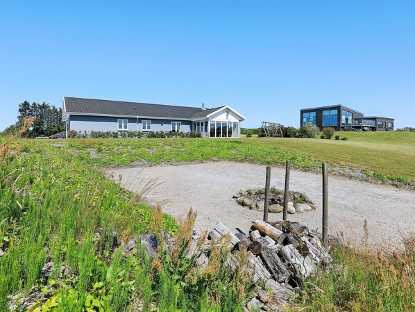 A modern house with a large patio area, surrounded by a grassy field and a gravel path. - 4 Star Holiday Home in Skals (Skals)