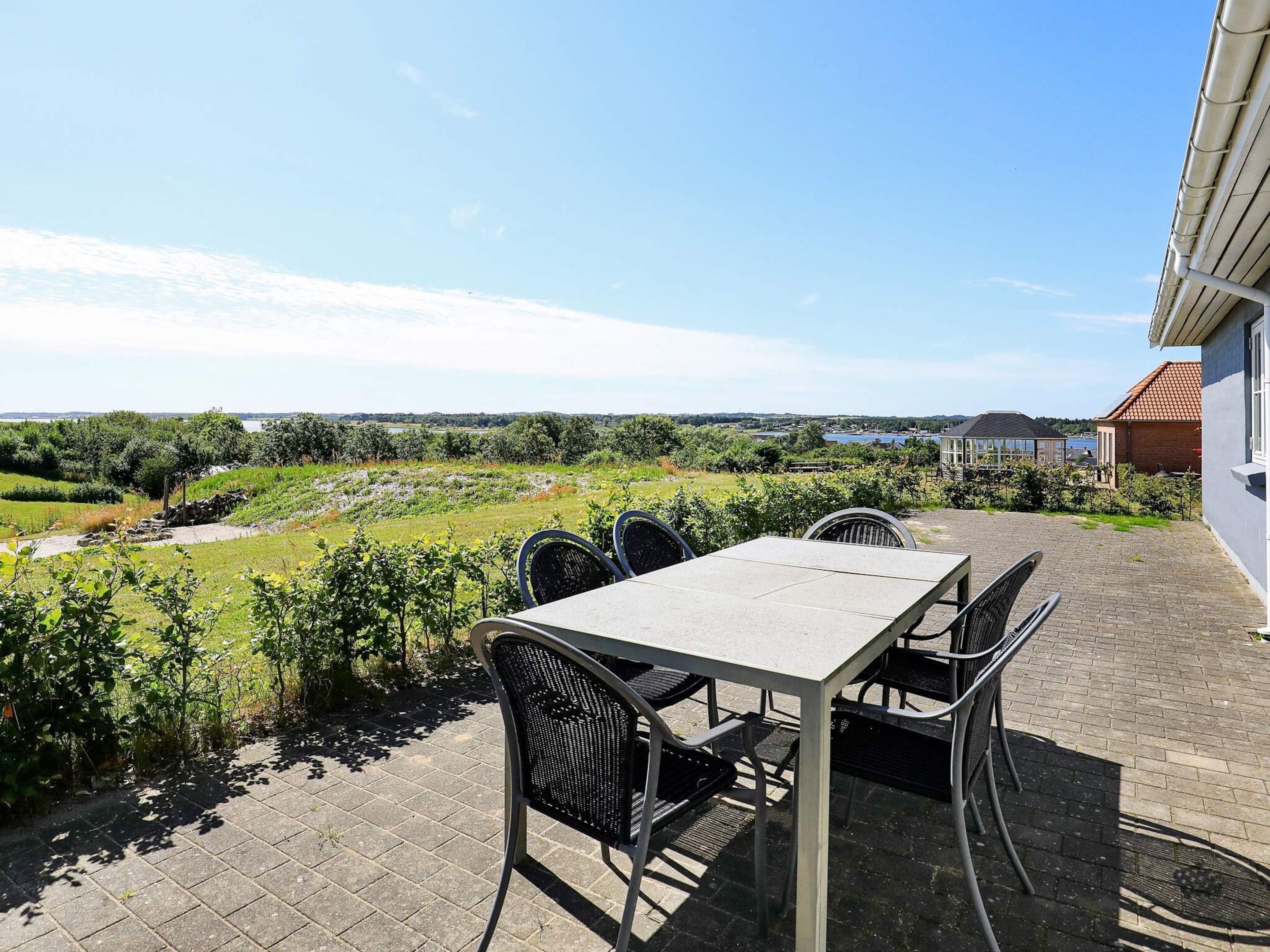 Un patio al aire libre con una mesa y sillas, vista a un paisaje verde y un edificio al fondo.