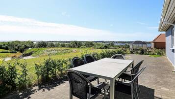 Un patio al aire libre con una mesa y sillas, vista a un paisaje verde y un edificio al fondo.