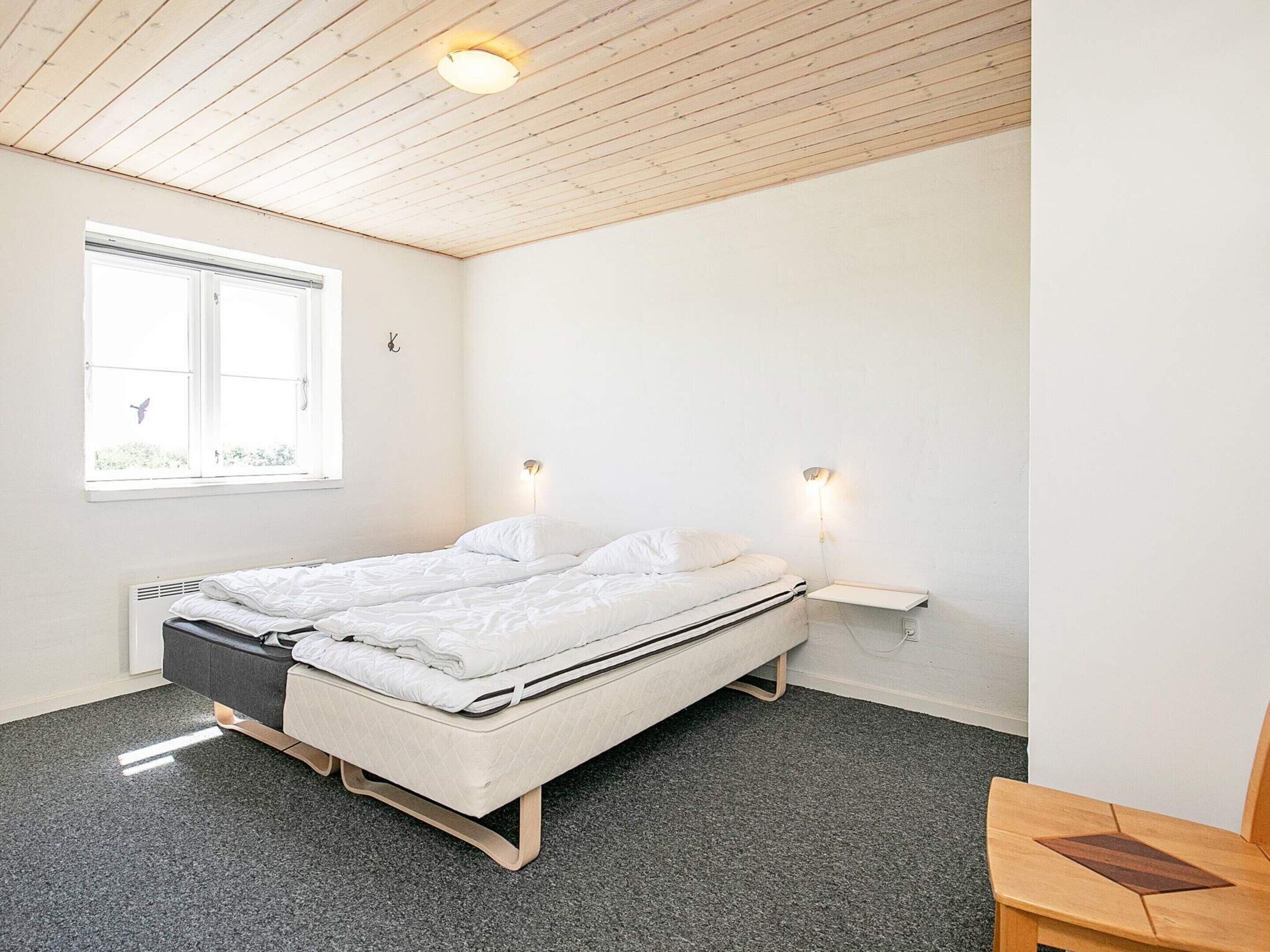 A minimalist bedroom with a single bed, a small table, and a window with a view of greenery.