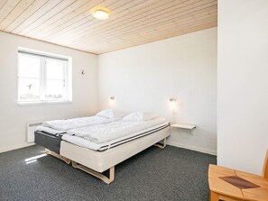 A minimalist bedroom with a single bed, a small table, and a window with a view of greenery. - 4 Star Holiday Home in Skals (Skals)