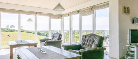 Una habitación con techo de madera, ventanas amplias, una mesa con vasos y un televisor.