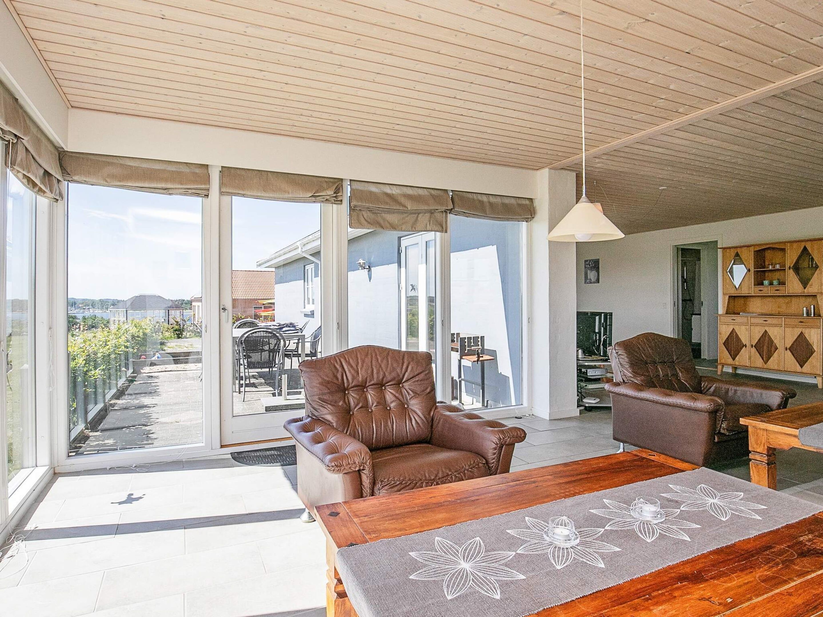 Un amplio salón con un sofá de cuero, una mesa de centro de madera y vistas a un patio exterior a través de puertas de cristal grandes.