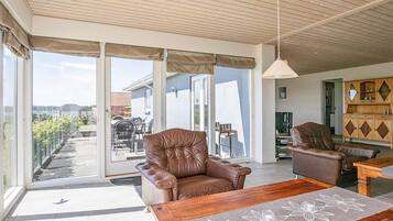 Un amplio salón con un sofá de cuero, una mesa de centro de madera y vistas a un patio exterior a través de puertas de cristal grandes.