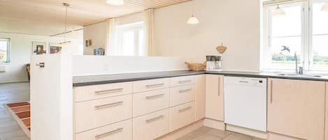 A modern kitchen with light wood cabinets, a black countertop, and a dishwasher.