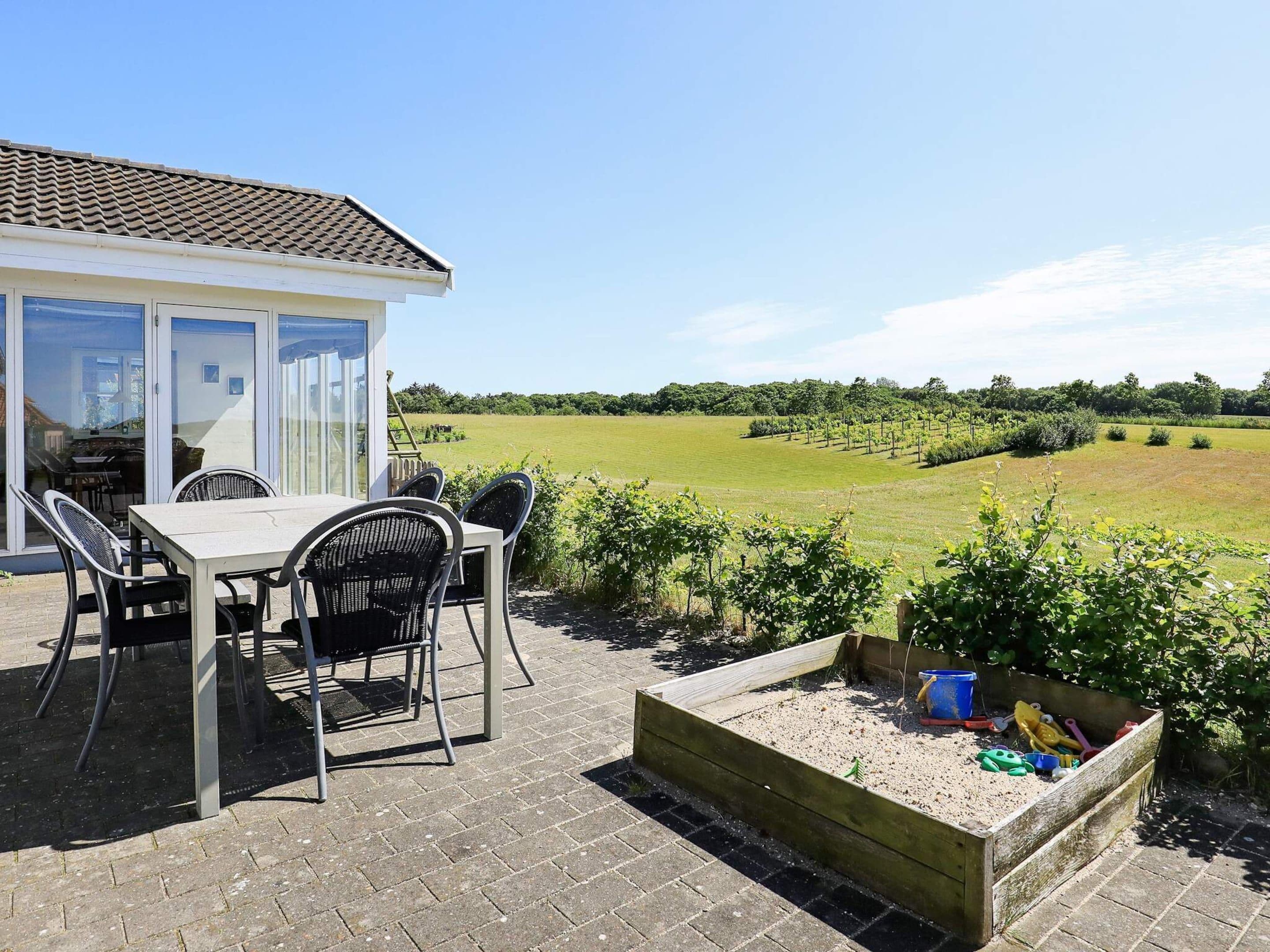 A patio with a table and chairs, a wooden play area, and a view of a green field.
