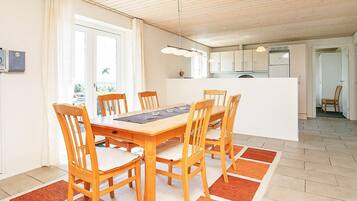 Un comedor con una mesa y sillas de madera, una cocina al fondo y vistas a través de una ventana.