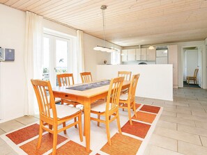 A dining area with a wooden table and chairs, a kitchen in the background, and a view through a window. - 4 Star Holiday Home in Skals (Skals)