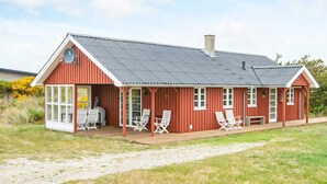 A red wooden building with a metal roof, large windows, and a covered porch with white chairs. - 6 Person Holiday Home in Hvide Sande-by Traum (Hvide Sande)