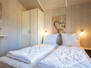 A bedroom with a bed, two white pillows, a quilted duvet, a wooden wardrobe, and a wall-mounted light fixture. - Holiday Home in GrÃ¶mmitz (Groemitz)