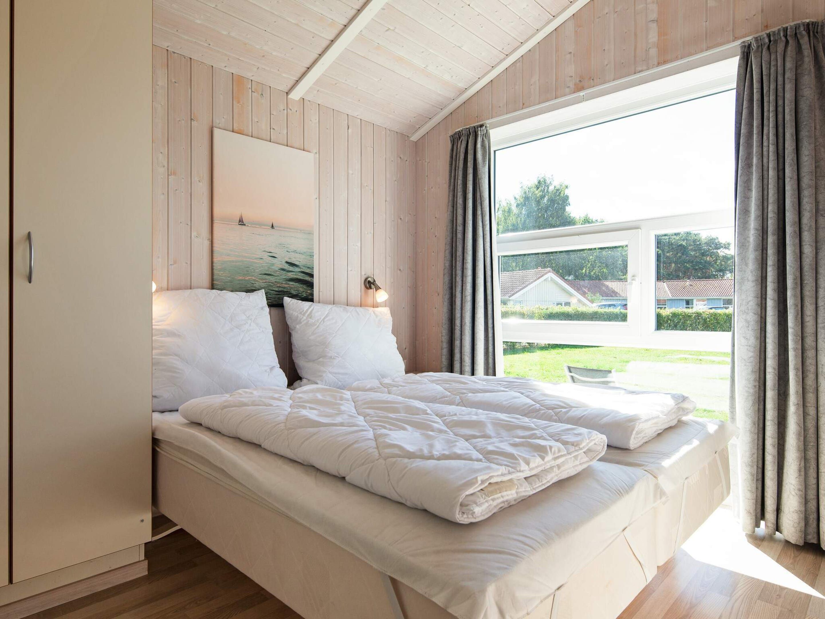 A bedroom with a bed, a nightstand, a painting, and a window with curtains.