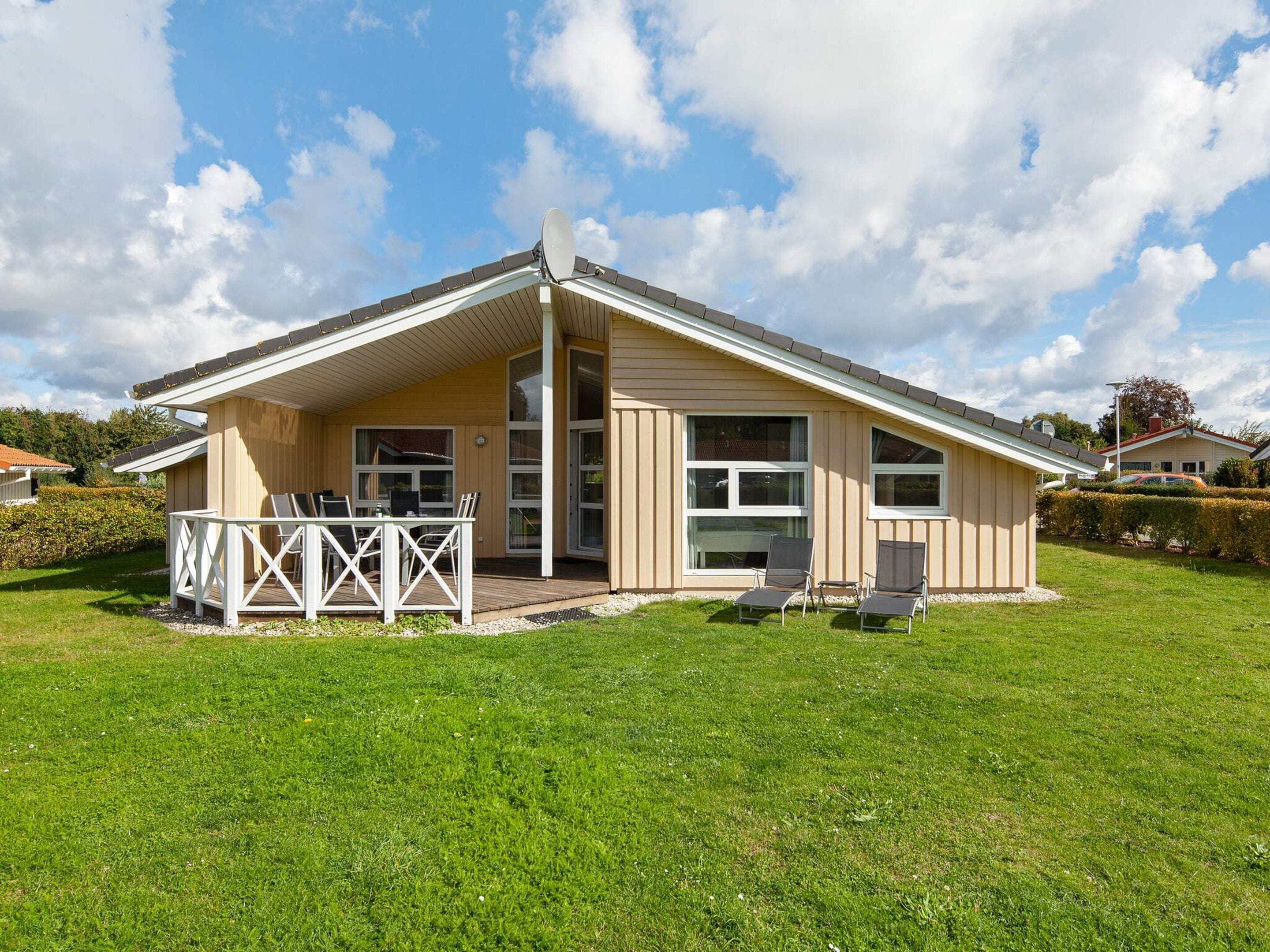 A single-story building with a covered patio area, a small deck, and a grassy lawn.