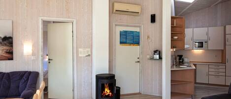 A room with a fireplace, wooden flooring, a kitchen area with a microwave, and a door with a sign.
