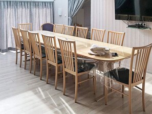 A dining area with a rectangular table surrounded by wooden chairs, a television mounted on the wall, and a glass partition. - Holiday Home in GrÃ¶mmitz (Groemitz)