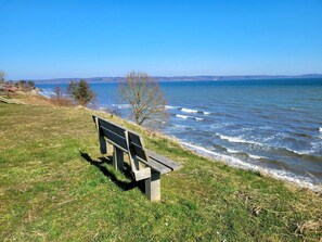 A bench by a lake with a clear view of the water and distant hills. - 6 Person Holiday Home in Borkop (Borkop)