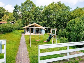 A covered outdoor seating area with a swing set, a brick pathway, and a white fence.