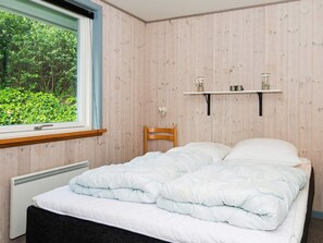 A bedroom with a bed, a window, a radiator, and a shelf with items.