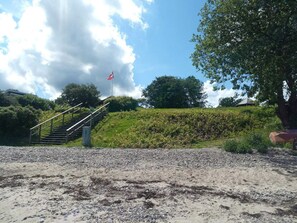 A gravel path leading to a staircase with a flag on top, surrounded by greenery and trees.