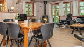 A cozy cabin interior with a wooden dining table, black leather chairs, a fireplace, and large windows offering a view of the outdoors. - 8 Person Holiday Home in Oksbol (Oksbol)