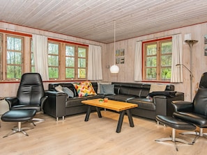 A spacious living room with a black leather sofa, two black leather chairs, a wooden coffee table, and large windows with curtains.