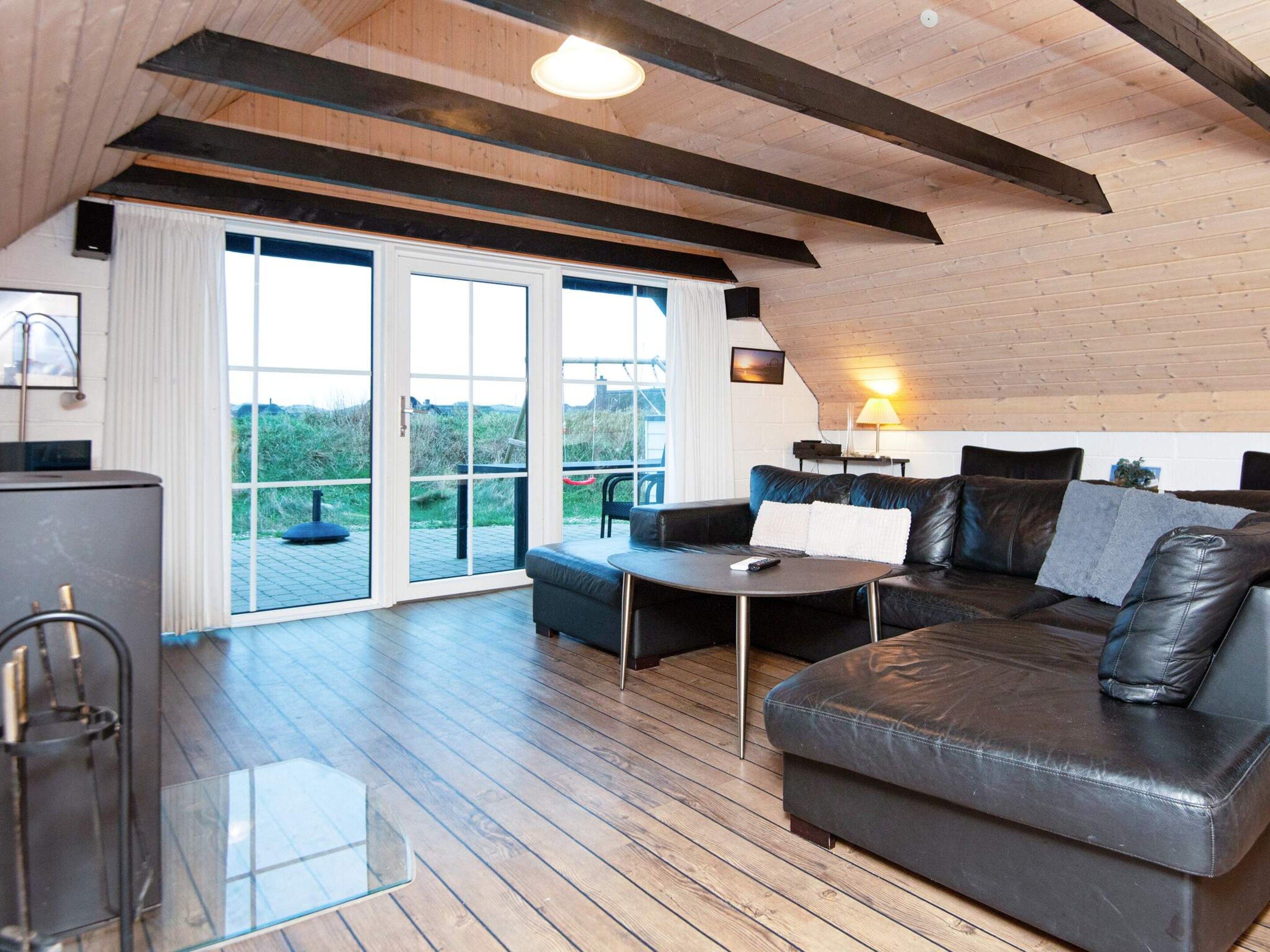 Un salon moderne avec un plafond en bois, un canapé en cuir, une table basse en verre et une vue sur l’extérieur grâce à de grandes portes coulissantes qui donnent sur un espace extérieur.