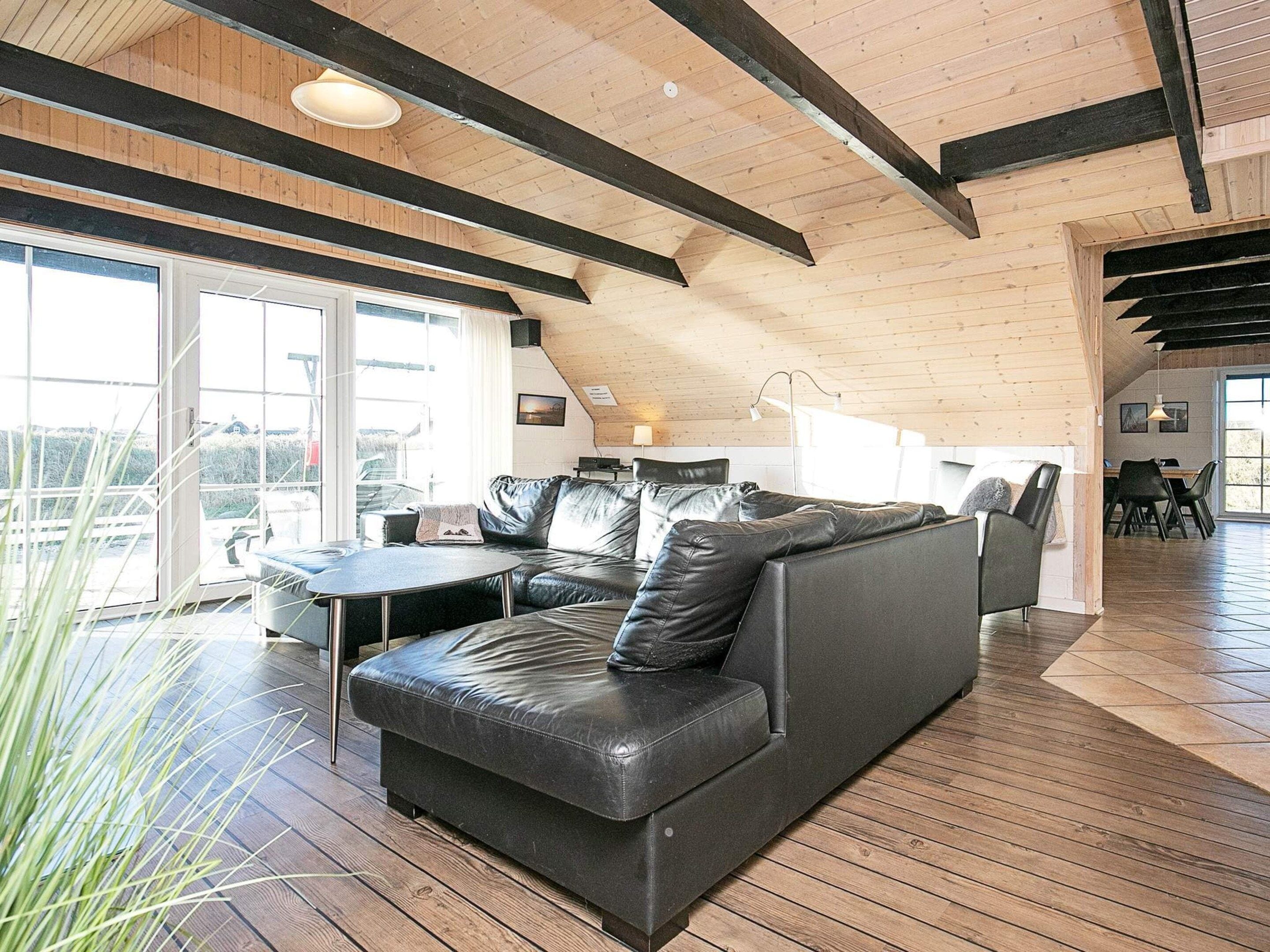 A modern interior with a leather sofa, wooden beams, and a dining area.