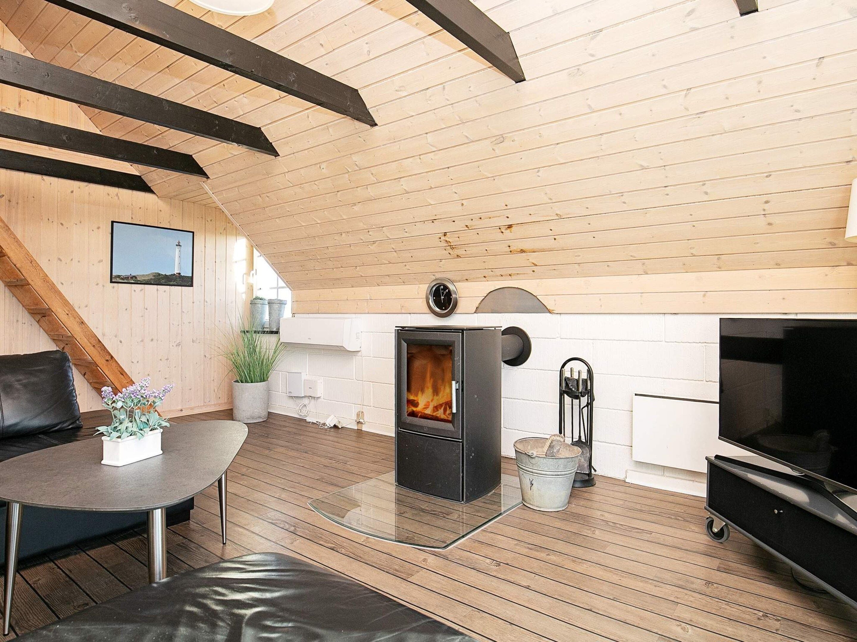 A cozy interior with a fireplace, wooden beams, a dining area, and a television.