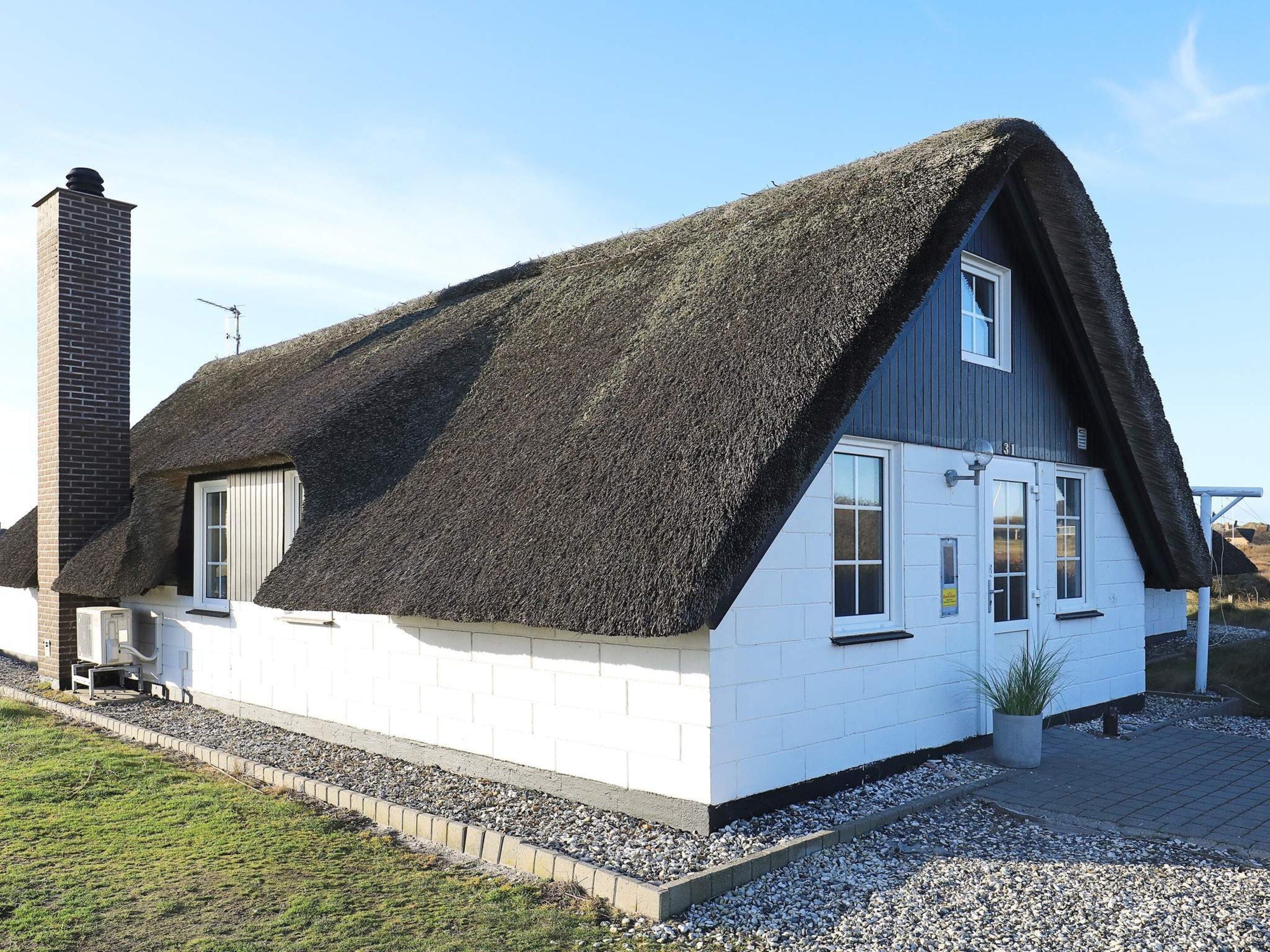 A house with a steeply pitched thatched roof, white exterior walls, and a chimney.