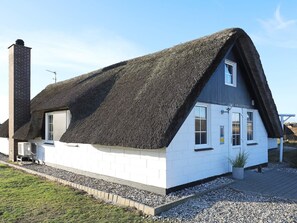 Et hus med et stejlt stråtækt tag, hvide ydermure og en skorsten.