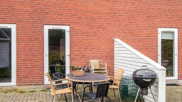 A brick house with a patio area featuring a round table and chairs, a grill, and a small garden.