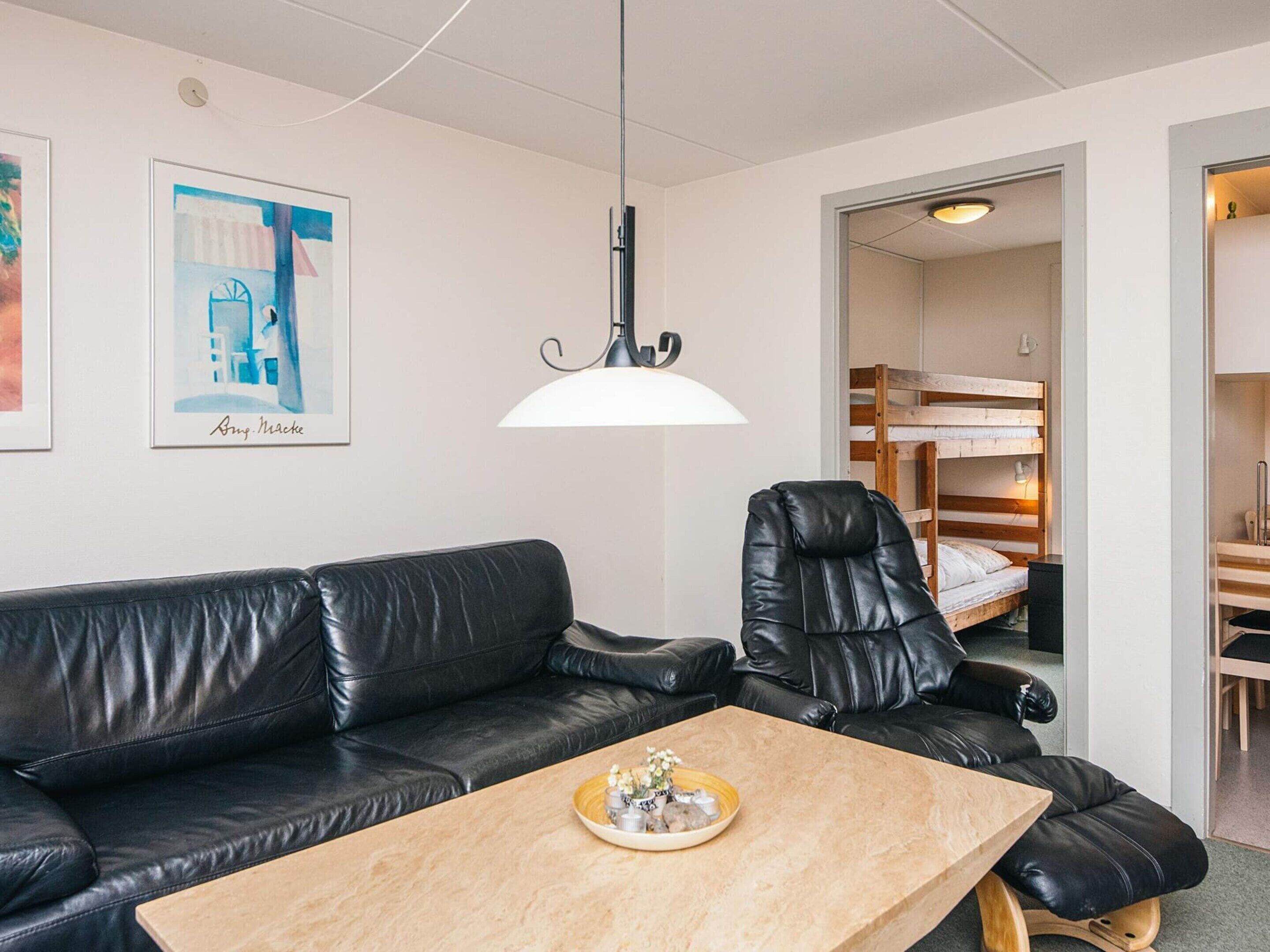 A room with a black leather sofa, a wooden coffee table, a black leather chair, a bunk bed, and a framed picture on the wall.