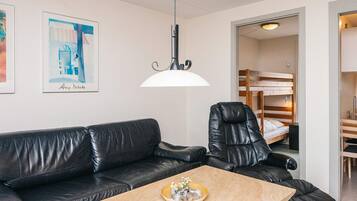 A room with a black leather sofa, a wooden coffee table, a black leather chair, a bunk bed, and a framed picture on the wall.