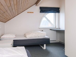 A bedroom with a sloped ceiling, a window with a view, a bed with a dark headboard, and a radiator.