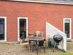 A brick house with a patio area featuring a round table and chairs, a grill, and a small garden.