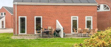 A red brick house with a sloped roof, a patio with outdoor furniture, and a small garden area.