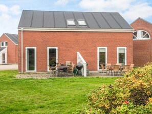 A red brick house with a sloped roof, a patio with outdoor furniture, and a small garden area.