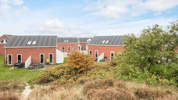 A row of brick buildings with flat roofs, a grassy area in front, and a tree to the right.