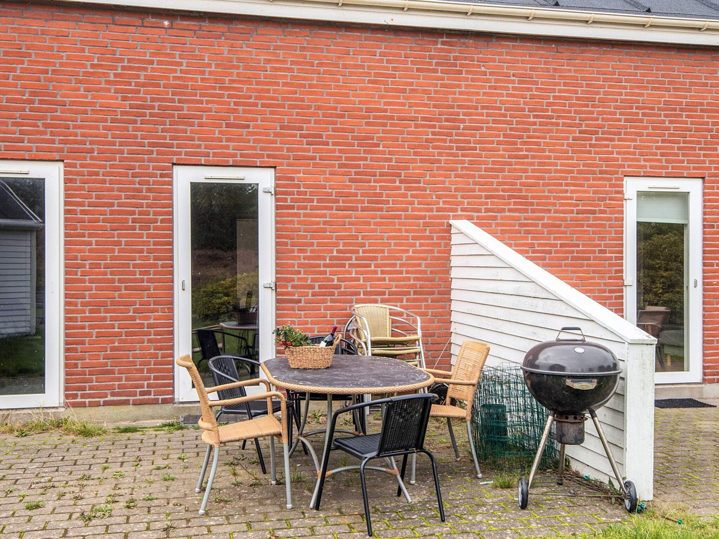 A brick house with a patio area featuring a round table, chairs, and a barbecue grill.