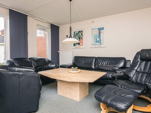 A modern living room with a black leather sofa, a wooden coffee table, and two framed artworks on the wall.